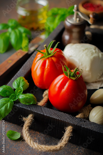 Ingredients for making traditional italian salad caprese in wooden box on dark slate or rusty metal background. Selective focus. Copy space.
