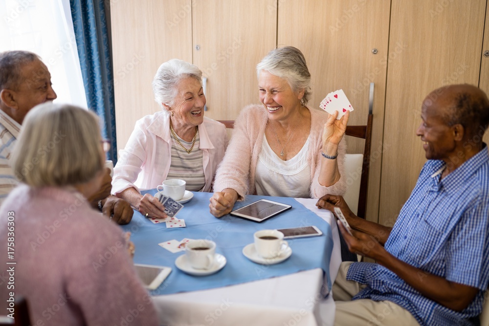 Obraz premium Happy senior people enjoying tea while playing cards