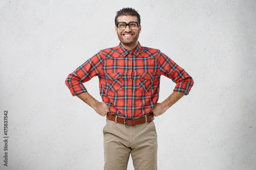 Positive smiling man keeps hands on waist, being confident in his victory. Young clumsy male wonk has happy expression as going to have first date with girlfriend, thinks what flowers to buy Positive smiling man keeps hands on waist, being confident in his victory. Young clumsy male wonk has happy expression as going to have first date with girlfriend, thinks what flowers to buy