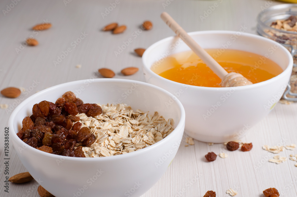Healthy Breakfast. Oatmeal with raisins in white bowl. Almonds, honey on white table background Healthy Breakfast. Oatmeal with raisins in white bowl. Almonds, honey on white table background