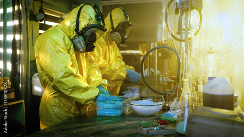 In the Underground Laboratory Two Clandestine Chemists Wearing Protective Masks and Coveralls Pack Bags of Synthesised Crystal Meth into Boxes for Further Distribution. photo