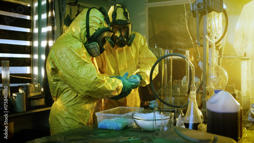 In the Underground Laboratory Two Clandestine Chemists Wearing Protective Masks and Coveralls Pack Bags of Synthesised Crystal Meth into Boxes for Further Distribution. photo