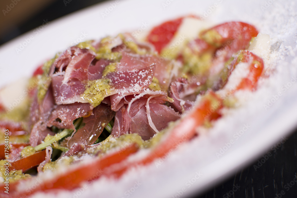 Delicious salad, prosciutto, and mozzarella cheese over dark background. Close up view of a delicious restaurant meal.