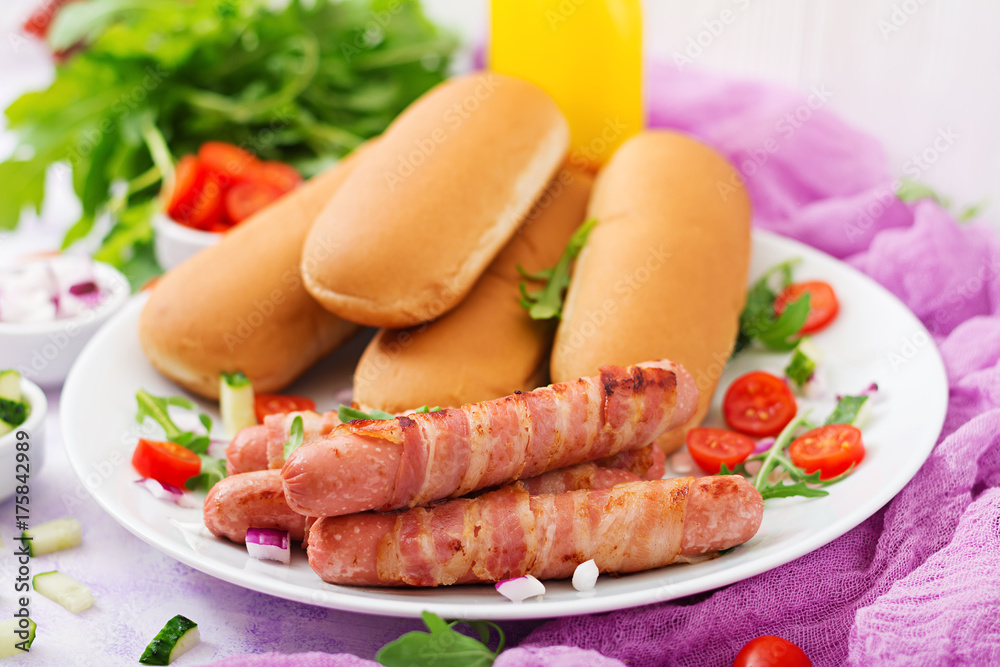 Ingredients for hot dog with sausage. bacon, cucumber, tomato and red onion on white plate Ingredients for hot dog with sausage. bacon, cucumber, tomato and red onion on white plate