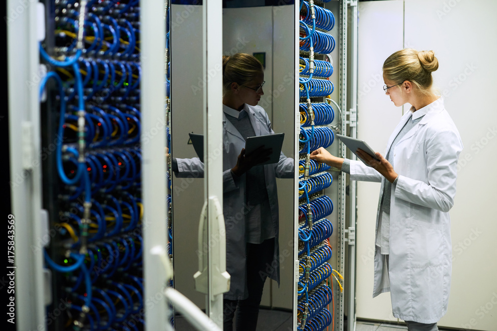 Portrait of young woman wearing lab coat working with servers in supercomputer research center, copy space