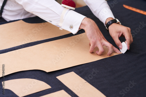 Closeup of tailors table with male hands tracing fabric making pattern for clothes in traditional atelier studio