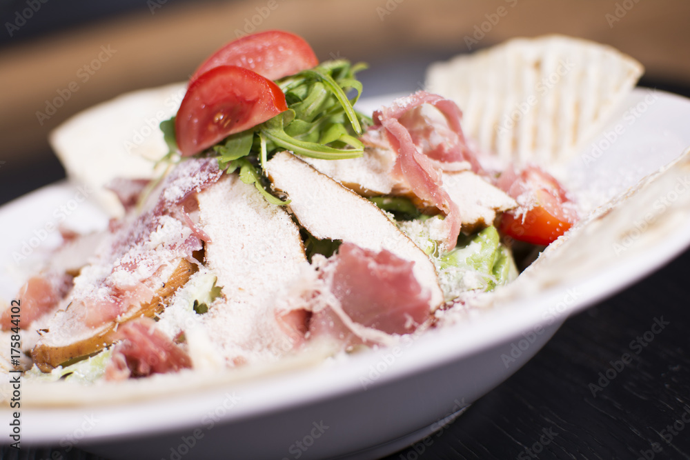 Salad with prosciutto and cheese on white plate close up. Served restaurant table. Delicious meal at a luxury restaurant.