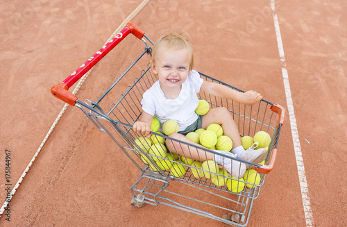 Obraz na płótnie The little girl sits in a basket for tennis balls. View from above w salonie