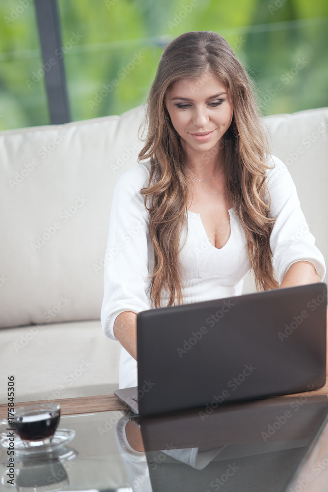 portrait of young woman sitting on sofa with laptop in summer house environment portrait of young woman sitting on sofa with laptop in summer house environment