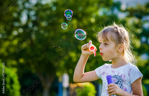 Close-up a little girl of six-years blowing beautiful soap bubbles outdoor.