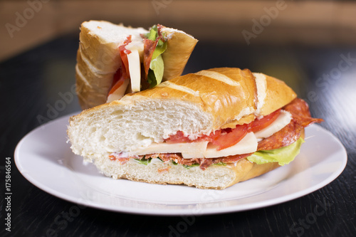 Fresh sandwich with ham, cheese, bacon, tomatoes, lettuce, cucumbers and onions on dark wooden background. Delicious restaurant meal.