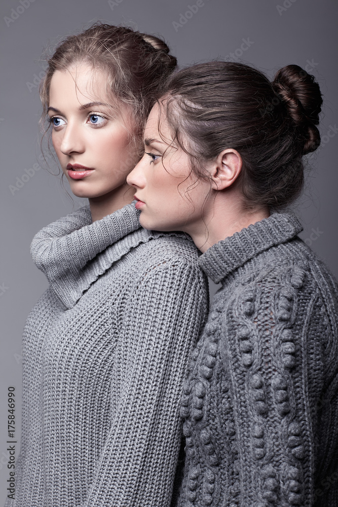 Two young women in gray sweaters on grey background. Beautiful girls stretching hands forward in embrace. Female friendship concept Two young women in gray sweaters on grey background. Beautiful girls stretching hands forward in embrace. Female friendship concept