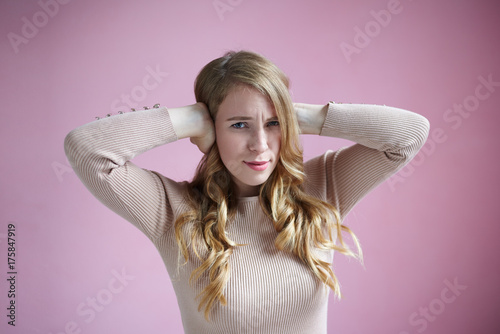 Isolated studio shot of stressed annoyed young European female covering ears with hands, having irritated painful look because of unbearable noise, sound of drill or loud music. Body language