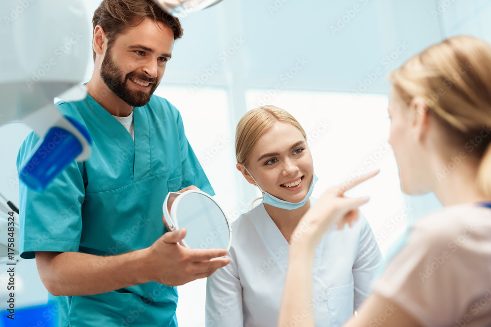Obraz premium A woman is sitting in a dental chair. Before her stands a doctor and holds a mirror in her hands. Near the nurse