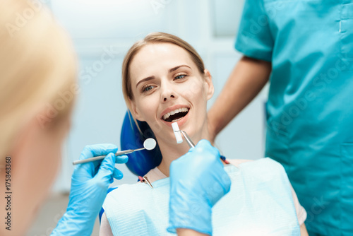 Dentists bent over a woman  whom they are treating teeth. She sits in the dental chair
