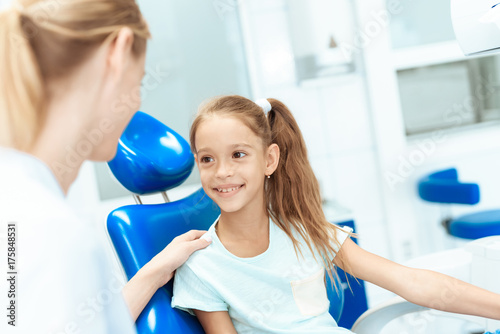 A little girl at a reception with a dentist. She sits in the dental chair and communicates with the dentist