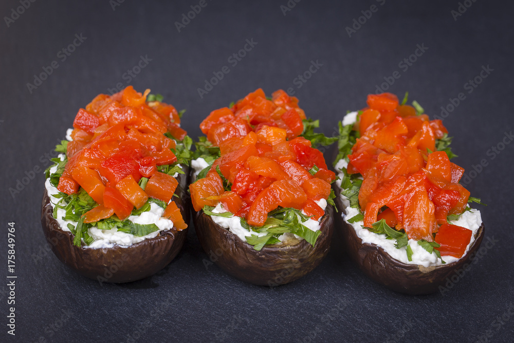 Baked eggplants stuffed with vegetable and cheese on a black slate background, close up Baked eggplants stuffed with vegetable and cheese on a black slate background, close up