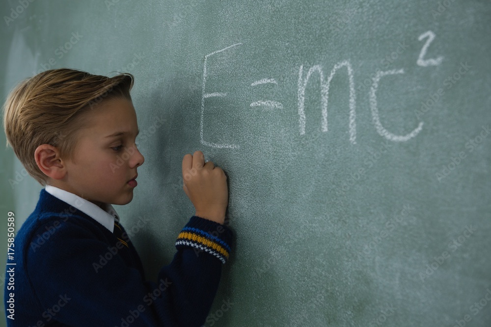 Schoolboy writing maths formula on chalkboard Schoolboy writing maths formula on chalkboard