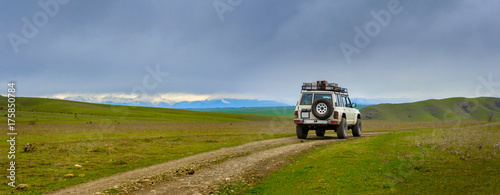 road in the mountains, in the distance one can see snowy peaks, on the road an off-road car