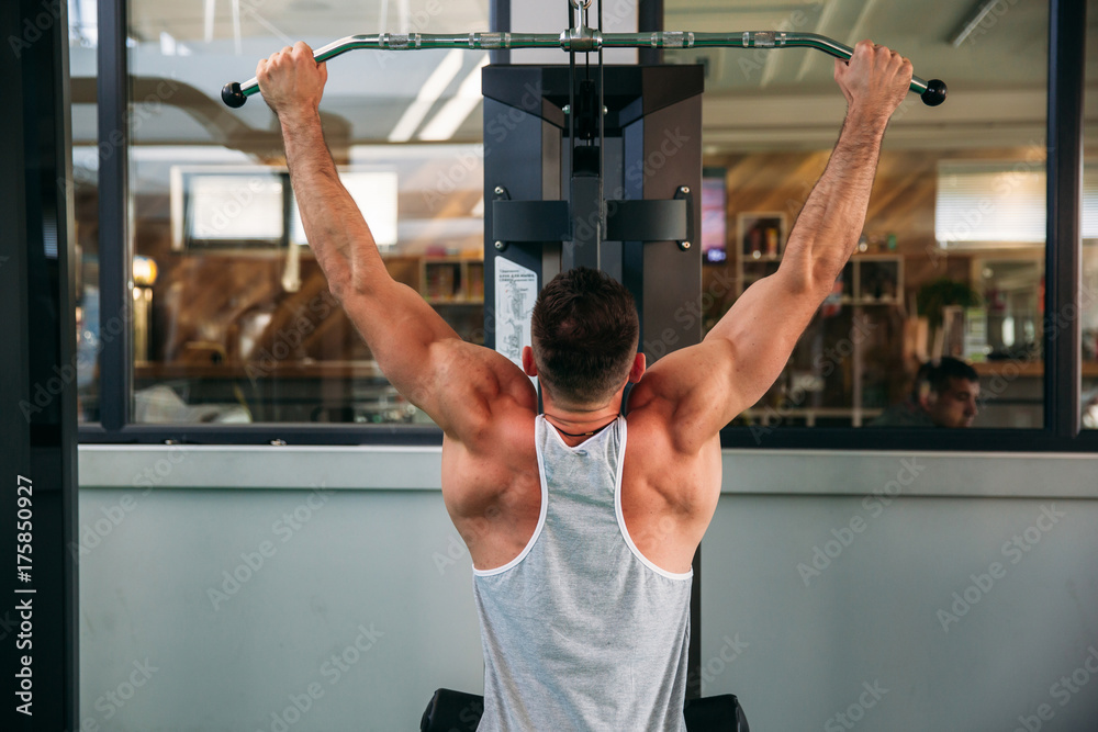 Fototapeta premium A young athlete trains in the gym. Shows the muscles of the back and chest