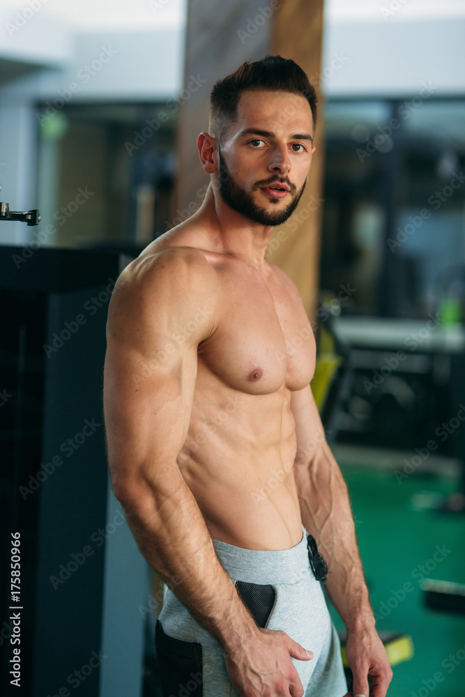 Fototapeta premium Young athlete posing with a torso for photography on a brick wall background. Bodybuilder, athlete with pumped muscles.