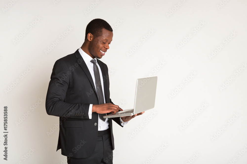 Black male smiling manager in suit standing, holding laptop at hands. Portrait