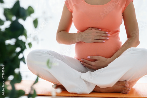 One european pregnant woman with pink tshirt do yoga exercises for carehealth her and unborn child in light bedroom at day time