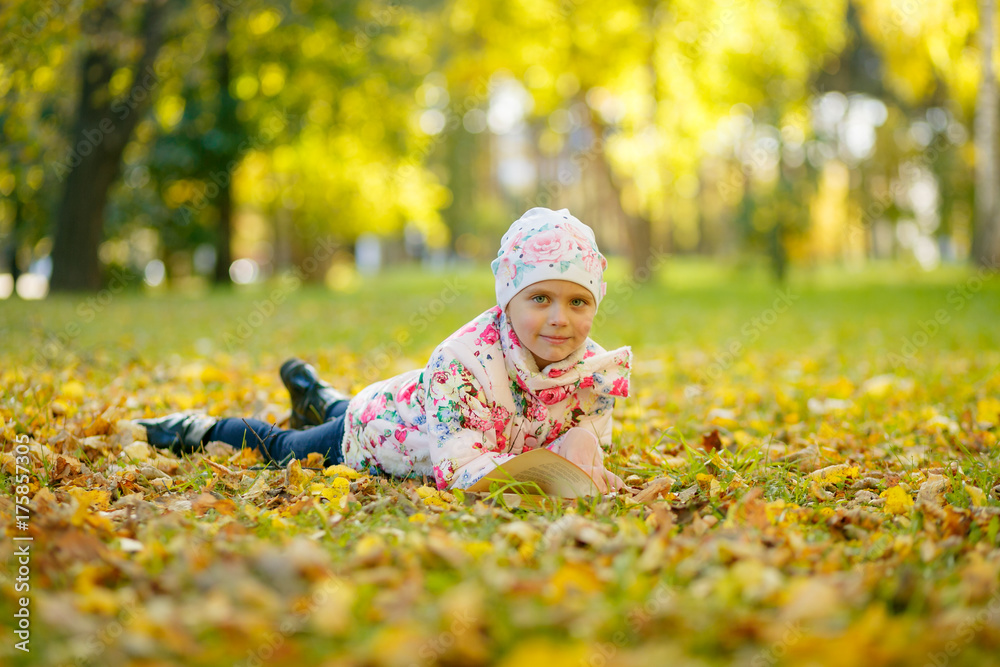 Cute little girl is reading a book while laying on yellow autumn leaves Cute little girl is reading a book while laying on yellow autumn leaves
