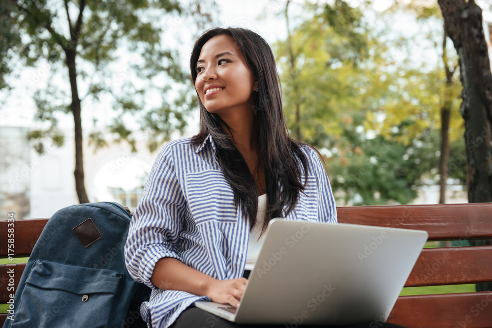 Portrait of young beautiful asian female student with laptop, sitting on wooden bench in park Portrait of young beautiful asian female student with laptop, sitting on wooden bench in park