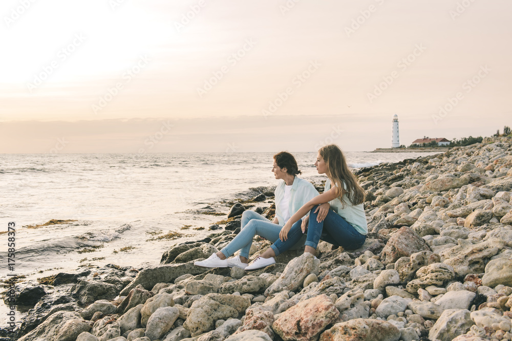 Mom and her teenage daughter relaxing together over sunset sea view