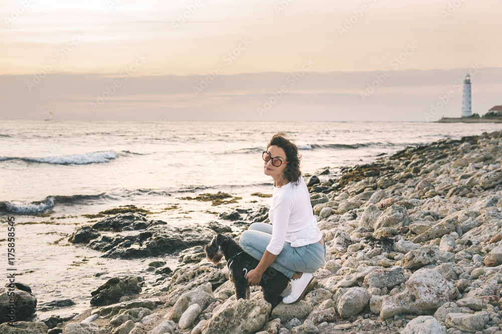 Beautiful girl playing her pet dog at the beach on sea shore.Woman walking with zwergschnauze.