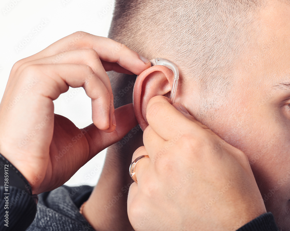 Fototapeta premium Young man hearing impaired dressing the hearing aid. At isolated white background.