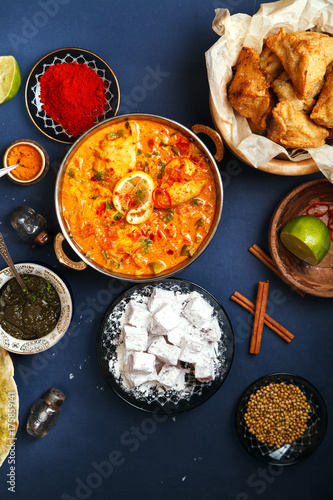 Indian cuisine on diwali holiday: tikka masala, samosa, patties and sweets with mint chutney and spices. Dark blue background. Vertical composition. Diwali celebration dinner