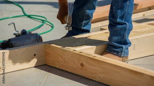 Worker Nails Framing in with Nail Gun and Hammer. a worker uses a nail gun to secure the joints of a wall for a home construction build
