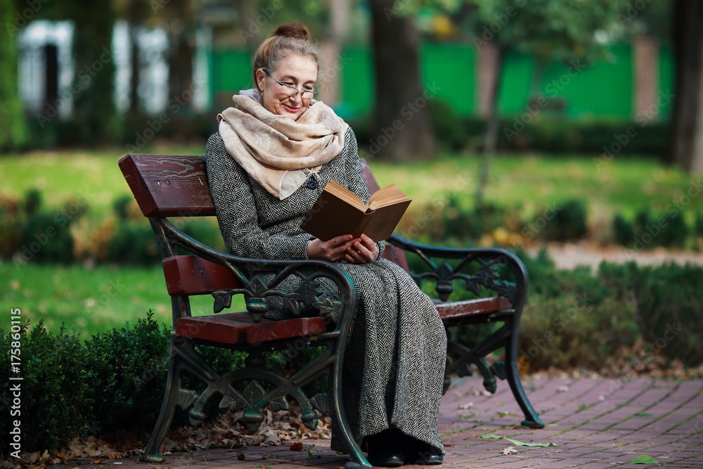 Счастливая старшая женщина, чтение книги в осеннем парке