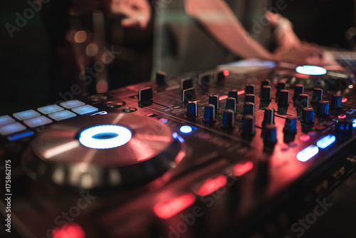 Hands of woman DJ tweak various track controls on dj's deck at night club 