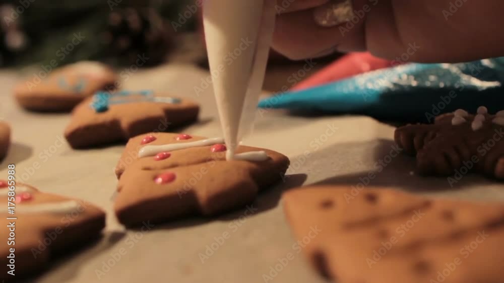Decoration process of Christmas cookies in motion. Close up woman garnishing with white icing homemade gingerbread fir tree near festive illuminate decor. Family culinary and traditions concept