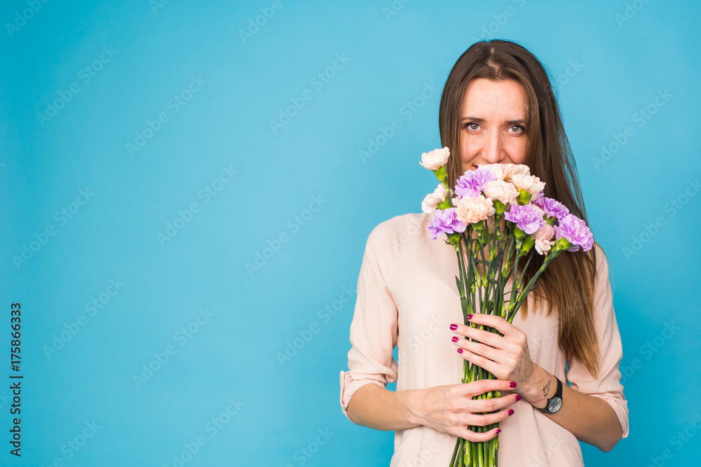 Beautiful young woman holding a bouquet of carnation flowers on a blue background, feminine, celebration
