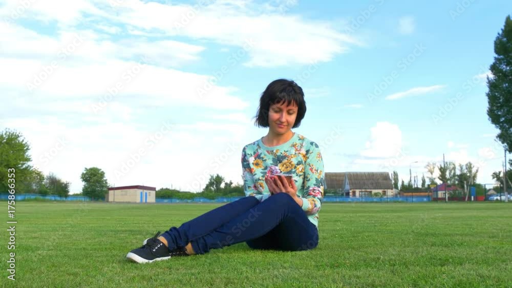 Attractive young woman on the lawn uses a smartphone at sunny day Attractive young woman on the lawn uses a smartphone at sunny day