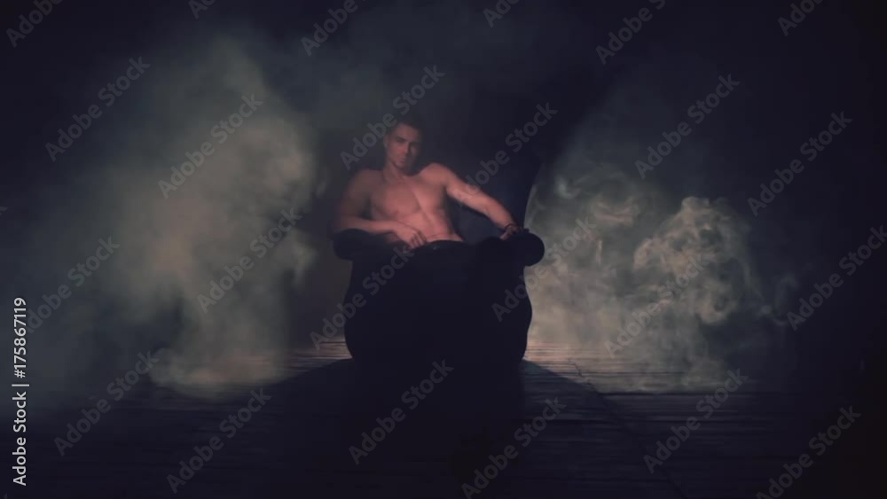 Sexy man sits in an armchair in smoke. The light appears and goes out Sexy man sits in an armchair in smoke. The light appears and goes out