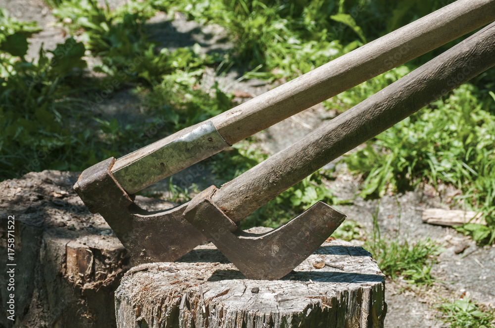 Old used weathered wooden axes stuck on wooden log for splitting wood into farmyard