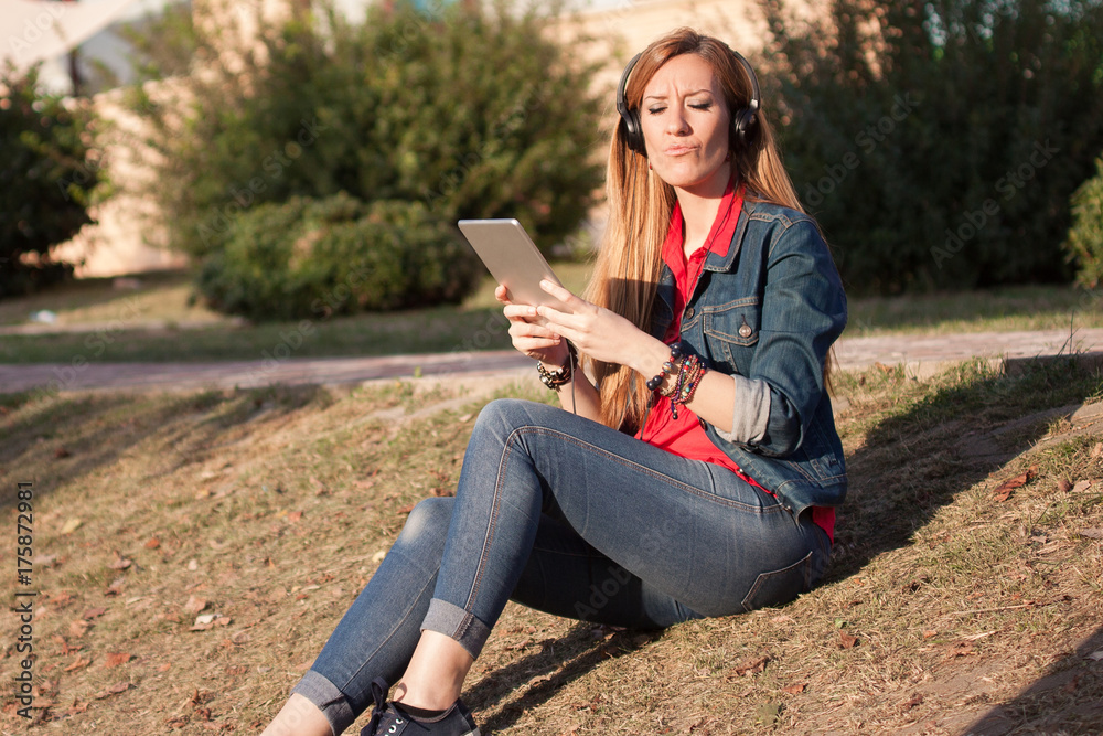 Fototapeta premium Young modern woman listening to music with headphones and smartphone smiling outdoors in the park