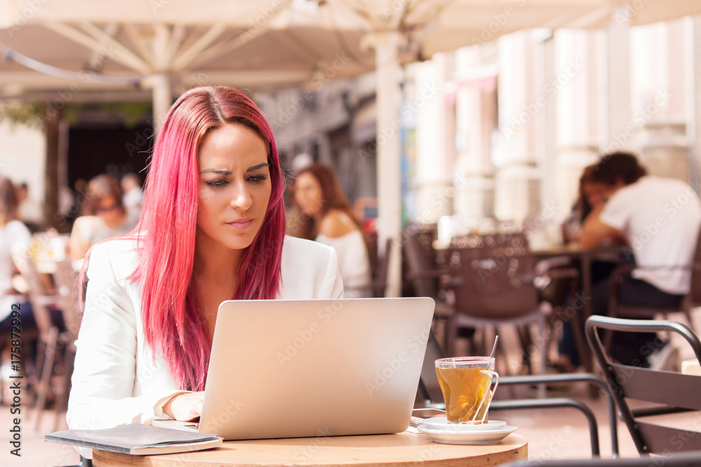 Young woman concentrated using a laptop at a table outside a cafe