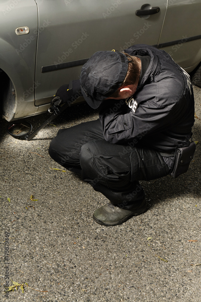 Police man checking car floor with inspection mirror for threats of bombs Police man checking car floor with inspection mirror for threats of bombs