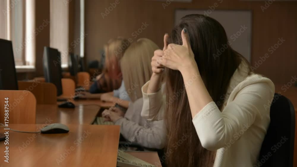 Business woman working on the computer. A group of young people in a computer classroom. Young brunette woman smiling straightens long hair Business woman working on the computer. A group of young people in a computer classroom. Young brunette woman smiling straightens long hair