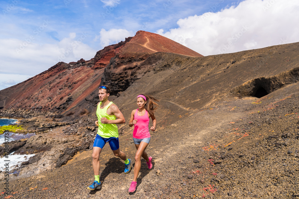 Running trail runners couple training on mountain. Ultra run race athletes training together on volcanic mountains nature landscape in summer outdoors. Difficult rocky terrain.