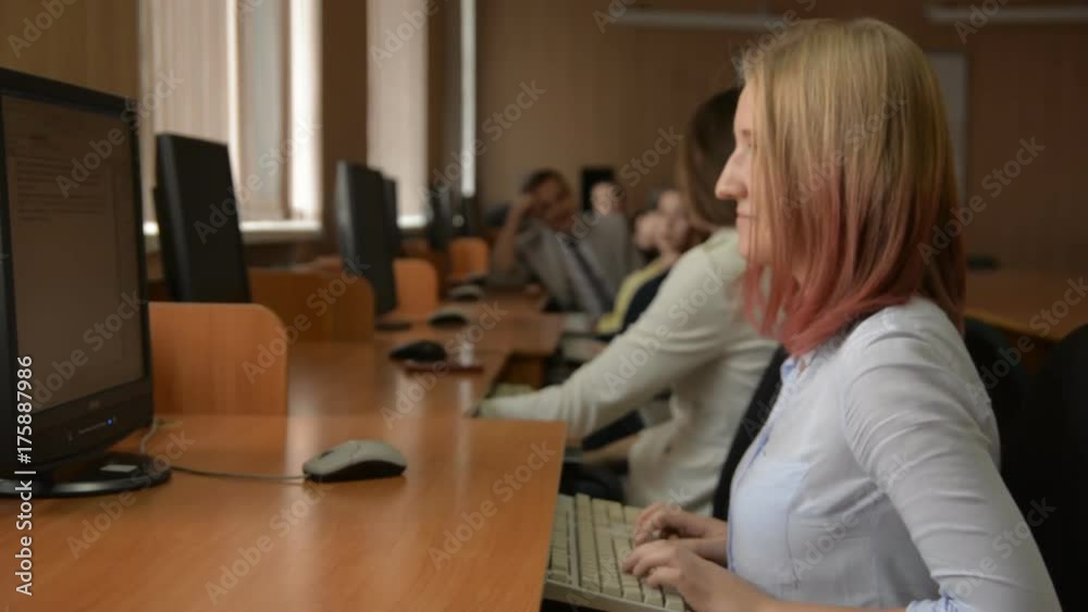 Cheerful student working on computer. A group of young people in a computer classroom. Young woman with blond hair smiling Cheerful student working on computer. A group of young people in a computer classroom. Young woman with blond hair smiling
