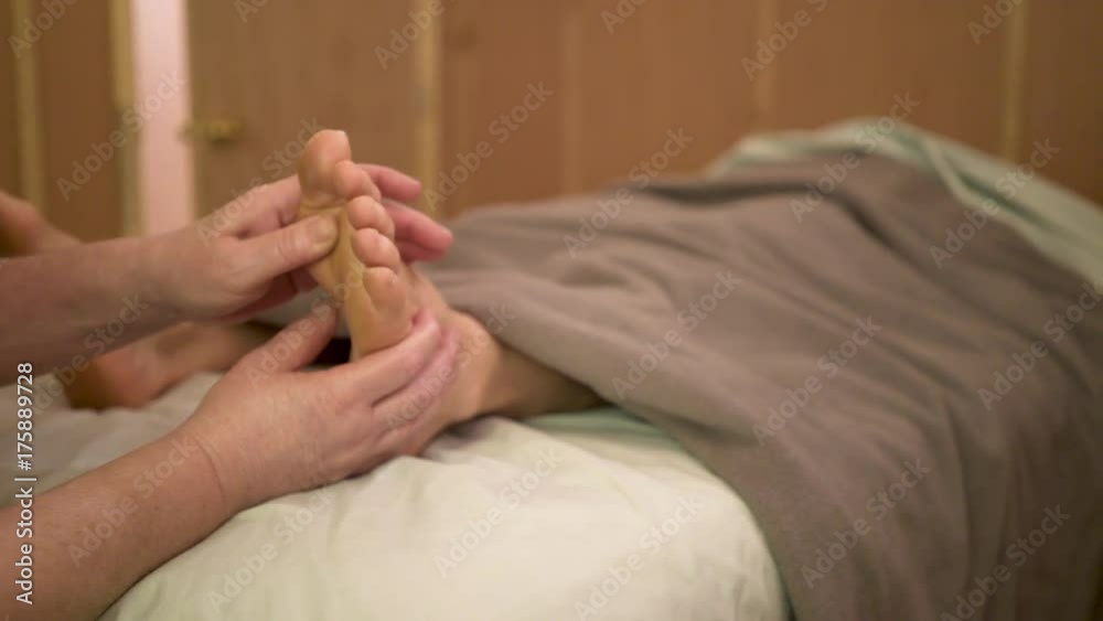 Using her thumbs, a massage therapist works balls of the feet of a caucasian woman for deep tissue massage. Using her thumbs, a massage therapist works balls of the feet of a caucasian woman for deep tissue massage.