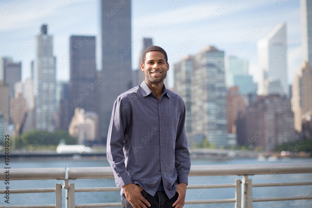Portrait of young handsome African American man smiling, with NYC skyline in the background Portrait of young handsome African American man smiling, with NYC skyline in the background
