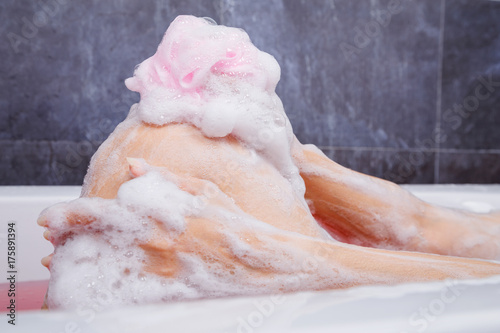 close up of woman washing knee with pink sponge in bathtub
